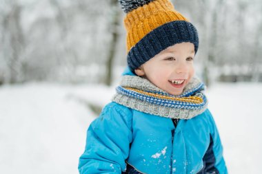 Sevimli küçük çocuk karlı kış gününde eğleniyor. Karda oynayan, kalın giysiler giymiş şirin bir çocuk. Çocuklu aileler için kış etkinlikleri.