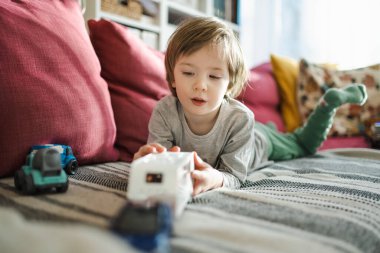 Oyuncak arabalarla oynayan şirin bir çocuk. Küçük çocuk oyuncaklarla eğleniyor. Çocuk evdeki sıcak bir oturma odasında vakit geçiriyor. Evde aile eğlencesi..