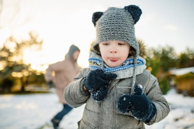 Sevimli küçük çocuk karlı kış gününde eğleniyor. Karda oynayan, kalın giysiler giymiş şirin bir çocuk. Çocuklu aileler için kış etkinlikleri.