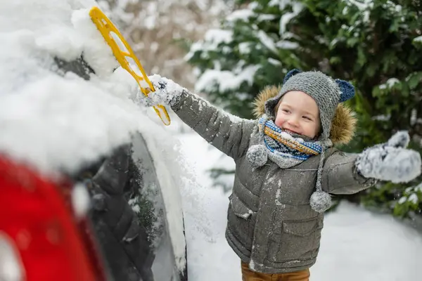 stock image Adorable little boy helping to brush a snow from a car. Mommy's little helper. Winter activities for small kids.