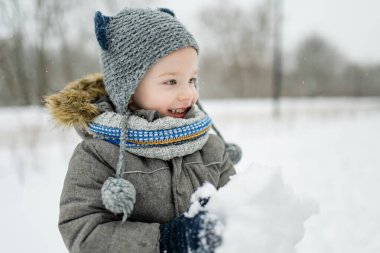 Sevimli küçük çocuk karlı kış gününde eğleniyor. Karda oynayan, kalın giysiler giymiş şirin bir çocuk. Çocuklu aileler için kış etkinlikleri.
