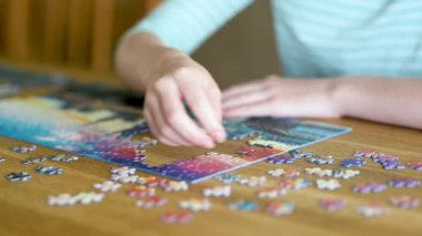Genç kadın ellerinin bulmaca çözerken yakın plan görüntüsü. Yapboz parçalarını birleştirmek, yapboz birleştirmek. Eğlenceli aile eğlencesi. Masa oyunları, evde rahatlama. Yavaş çekim görüntüleri.