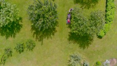 Arka bahçede elektrikli çim biçme makinesi ya da benzin çim biçme makinesiyle çim biçen bir adamın havadan aşağı görüntüsü. Bahçıvanlık malzemeleri ve ekipmanlar. Çim biçme makinesiyle çim biçme işlemi.