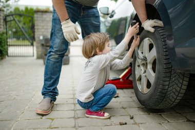 Küçük tatlı çocuk, babasının arka bahçesinde araba tekerleklerini değiştirmesine yardım ediyor. Baba küçük oğluna alet kullanmayı öğretiyor. Küçük bir çocuğun aktif ebeveyni.