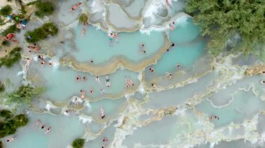 Terme di Saturnia 'nın yukarıdan aşağıya hava manzarası, jeotermal sülfür yayları ve Saturnia termal banyolarında şelaleli doğal spa. Cascate del Mulino, Grosseto, Toskana, İtalya 'da yıkanan insanlar.