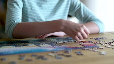 Genç kadın ellerinin bulmaca çözerken yakın plan görüntüsü. Yapboz parçalarını birleştirmek, yapboz birleştirmek. Eğlenceli aile eğlencesi. Masa oyunları, evde rahatlama. Yavaş çekim görüntüleri.