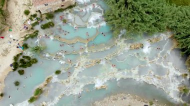Terme di Saturnia 'nın yukarıdan aşağıya hava manzarası, jeotermal sülfür yayları ve Saturnia termal banyolarında şelaleli doğal spa. Cascate del Mulino, Grosseto, Toskana, İtalya 'da yıkanan insanlar.