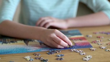 Genç kadın ellerinin bulmaca çözerken yakın plan görüntüsü. Yapboz parçalarını birleştirmek, yapboz birleştirmek. Eğlenceli aile eğlencesi. Masa oyunları, evde rahatlama. Yavaş çekim görüntüleri.