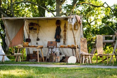 Ortaçağ aletleri, silahlar ve el yapımı eşyalar, antik zanaatkarlık ve günlük yaşamın sergilendiği bir arkeoloji festivalinde, bir çadırın altındaki ahşap masalarda sergileniyor..