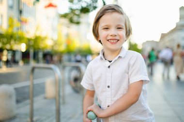Güneşli bir yaz akşamında güzel bir çocuk mobiletiyle şehirde geziyor. Paten süren küçük bir çocuk. Çocuklar için aktif eğlence ve açık hava sporları.