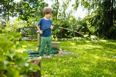 Sıcak bir yaz gününde bahçe hortumuyla oynayan tatlı bir çocuk. Çocuk yazın suyla oynuyor. Küçük çocuklarla aktif eğlence..