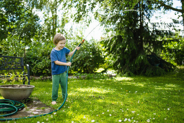 Cute little boy playing with garden hose on hot summer day. Child playing with water at summertime. Active leisure with little kids.