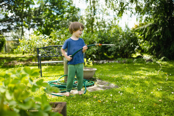 Cute little boy playing with garden hose on hot summer day. Child playing with water at summertime. Active leisure with little kids.