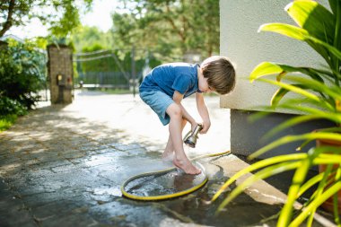 Sıcak bir yaz gününde bahçe hortumuyla oynayan tatlı bir çocuk. Çocuk yazın suyla oynuyor. Küçük çocuklarla aktif eğlence..