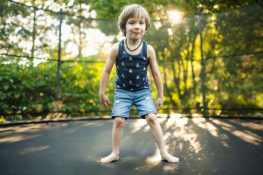 Sıcak ve güneşli bir yaz gününde, bir bahçede trambolinde zıplayan sevimli bir çocuk. Çocuklar için spor ve egzersiz. Yazın açık hava eğlence aktiviteleri.