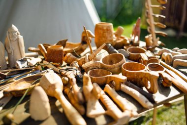 Geleneksel işçilik ve günlük yaşamı yansıtan bir arkeolojik ortaçağ festivalinde çeşitli el yapımı ahşap çatal bıçaklar, figürler ve aletler bir masada sergileniyor..
