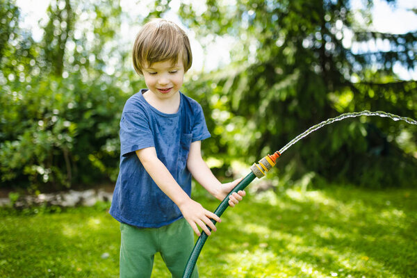 Cute little boy playing with garden hose on hot summer day. Child playing with water at summertime. Active leisure with little kids.