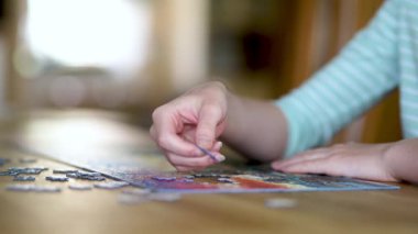 Genç kadın ellerinin bulmaca çözerken yakın plan görüntüsü. Yapboz parçalarını birleştirmek, yapboz birleştirmek. Eğlenceli aile eğlencesi. Masa oyunları, evde rahatlama. Yavaş çekim görüntüleri.