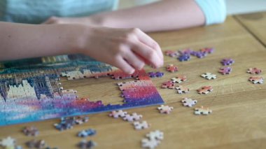 Genç kadın ellerinin bulmaca çözerken yakın plan görüntüsü. Yapboz parçalarını birleştirmek, yapboz birleştirmek. Eğlenceli aile eğlencesi. Masa oyunları, evde rahatlama. Yavaş çekim görüntüleri.