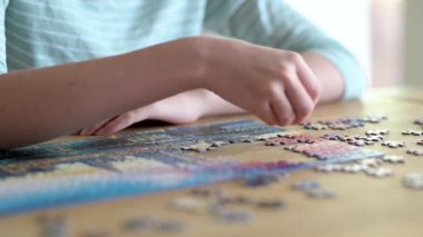 Genç kadın ellerinin bulmaca çözerken yakın plan görüntüsü. Yapboz parçalarını birleştirmek, yapboz birleştirmek. Eğlenceli aile eğlencesi. Masa oyunları, evde rahatlama. Yavaş çekim görüntüleri.