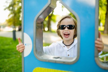 Güneş gözlüklü şık bir genç çocuk Litvanya 'nın Vilnius kentindeki güneşli bir parkta modern bir su çeşmesinden su içiyor.