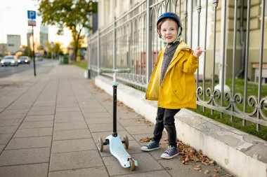 Güneşli bir sonbahar akşamında küçük sevimli bir çocuk mobiletini güneşli bir şehirde sürüyor. Paten süren küçük bir çocuk. Çocuklar için aktif eğlence ve açık hava sporları.
