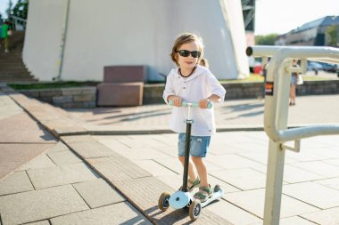Güneşli bir yaz akşamında küçük sevimli bir çocuk mobiletiyle şehirde geziyor. Paten süren küçük bir çocuk. Çocuklar için aktif eğlence ve açık hava sporları.