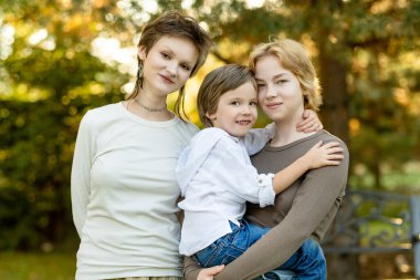 Üç kardeş, güneşli bir bahçede sevgi, birlik ve birlikte büyümenin sevincini yakaladıkları bir anı paylaşıyorlar.
