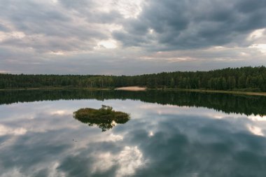 Litvanya 'daki Gela Gölü sakin sularındaki dramatik bulutları ve ormanı yansıtarak sakin ve karamsar bir manzara yaratır.