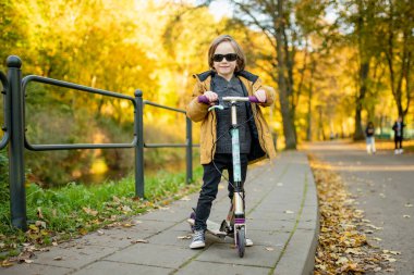 Güneşli bir sonbahar akşamında küçük sevimli bir çocuk mobiletini güneşli bir şehirde sürüyor. Paten süren küçük bir çocuk. Çocuklar için aktif eğlence ve açık hava sporları.