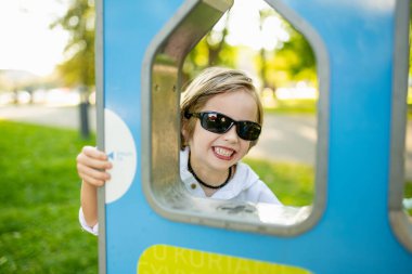 Güneş gözlüklü şık bir genç çocuk Litvanya 'nın Vilnius kentindeki güneşli bir parkta modern bir su çeşmesinden su içiyor.