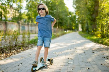 Güneşli bir yaz akşamında küçük sevimli bir çocuk mobiletiyle şehirde geziyor. Paten süren küçük bir çocuk. Çocuklar için aktif eğlence ve açık hava sporları.