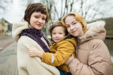 Sıcak ceketli üç kardeş bulutlu bir kış gününde dışarıda yan yana poz veriyorlar.