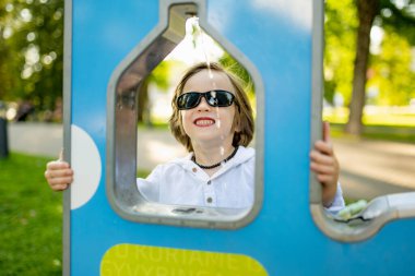 Güneş gözlüklü şık bir genç çocuk Litvanya 'nın Vilnius kentindeki güneşli bir parkta modern bir su çeşmesinden su içiyor.