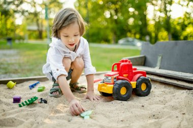 Parlak güneşli bir yaz gününde oyun alanında eğlenen sevimli küçük çocuk. Kum havuzunda plastik kamyonla oynayan sevimli bir çocuk. Çocuklu aileler için açık hava aktiviteleri.
