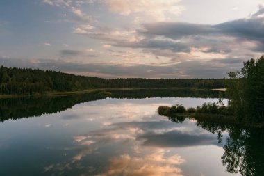 Litvanya 'daki Gela Gölü sakin sularındaki dramatik bulutları ve ormanı yansıtarak sakin ve karamsar bir manzara yaratır.