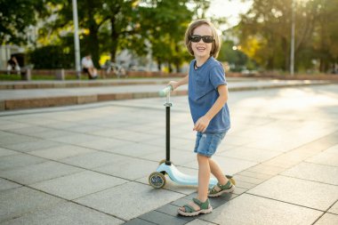 Güneşli bir yaz akşamında küçük sevimli bir çocuk mobiletiyle şehirde geziyor. Paten süren küçük bir çocuk. Çocuklar için aktif eğlence ve açık hava sporları.