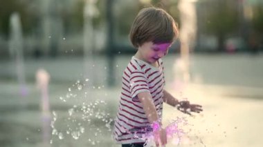 Küçük şirin çocuk şehir çeşmesinde suyla eğleniyor. Çocuk sıcak bir günde dışarıda su oyunu oynuyor. Küçük çocuklar için kentsel yaz aktiviteleri. Yavaş çekim görüntüleri.