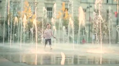 Küçük şirin çocuk şehir çeşmesinde suyla eğleniyor. Çocuk sıcak bir günde dışarıda su oyunu oynuyor. Küçük çocuklar için kentsel yaz aktiviteleri. Yavaş çekim görüntüleri.
