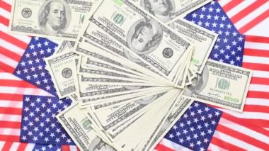 100 dolarlık banknotların ve Amerikan bayrağının döndüğü bir arka plan.