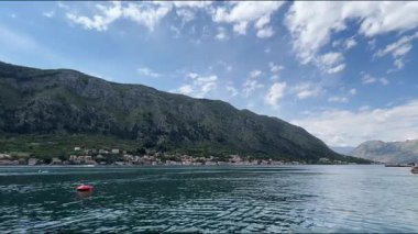 Karadağ 'ın Kotor Körfezi' nin huzurlu manzarası, kıyı köylerinin, yumuşak bulutlarla dolu bir gökyüzünün altında yeşil dağlar ve mavi sularla buluştuğu yer..
