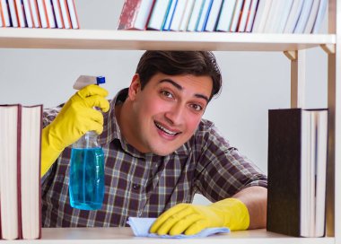 Kitap rafından toz temizleyen adam.