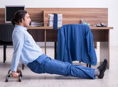 Genç yakışıklı işadamı iş yerinde egzersiz yapıyor.