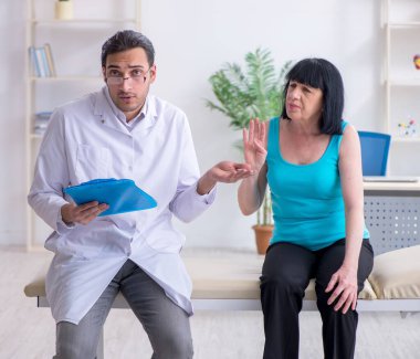 Genç erkek doktor yaşlı kadın hastayı muayene ediyor.