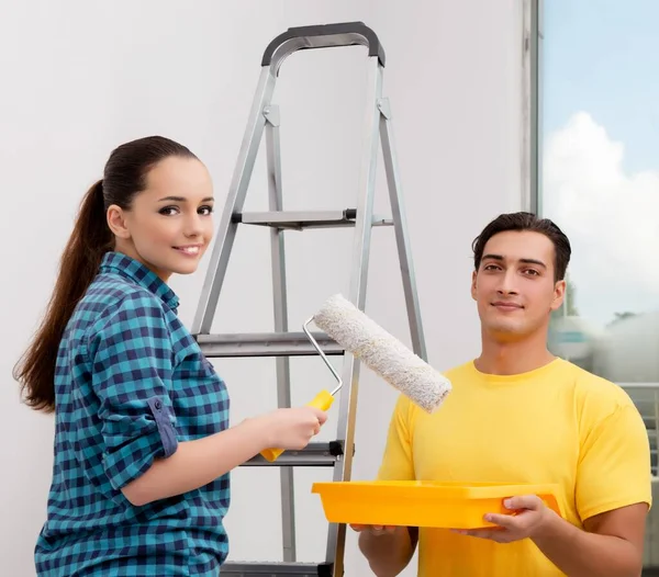 The young couple painting wall at home