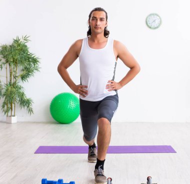 Genç yakışıklı adam içeride spor egzersizleri yapıyor.