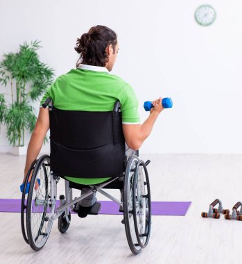 Tekerlekli sandalyedeki genç adam içeride egzersiz yapıyor.