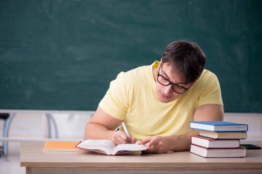 Genç öğrenci yeşil panonun önünde oturuyor.