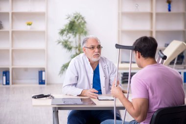 Genç bacağı yaralı hasta yaşlı doktoru ziyaret ediyor.