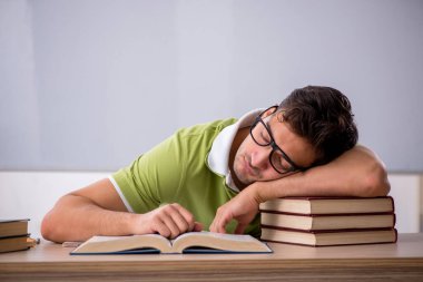 Sınıfta beyaz tahtanın önünde oturan genç öğrenci.